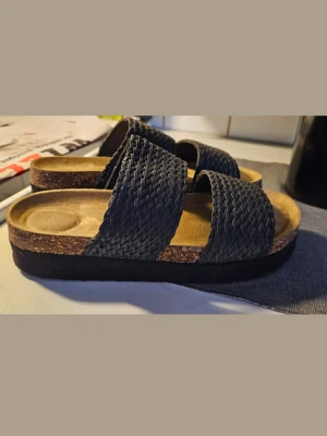 Svarta sandaler med flätade remmar - Svarta sandaler med två breda flätade remmar över foten. Sulan är platt och något högre. Endast testade 