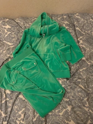 Gröna mjukisbyxor i velour - Säljer ett par gröna mjukisbyxor i mjuk velour med bred resår i midjan och stora fickor med lock bak. Byxorna har en relaxed passform och är perfekta för chill dagar. Matchar med hoodie i samma material för en komplett look. Man ser även små vita fläckar på ena benet därav priset för setet  