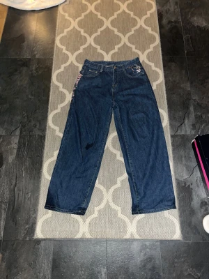 Wide jeans från Derschutze med broderi - Unika mörkblå jeans från Derschutze med bred passform och hög midja. På bakfickan finns ett snyggt broderi med rosa och vita blommor som ger en cool och personlig vibe. Klassisk femficksmodell i jeansmaterial, perfekt för dig som gillar statement-plagg.