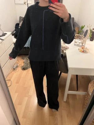 Mörkblå stickad tröja med kontrastsömmar - Mörkblå stickad tröja från Zara med ribbad midja och ärmslut. Tröjan har tunna ljusblå kontrastsömmar längs ärmar och mitt fram samt bak, vilket ger en clean och modern vibe. Rund halsringning och långärmad modell, perfekt för lager på lager under kyliga dagar. Tröjan är i storleken S