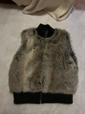 Grå pälsväst - Snygg grå pälsväst från saint tropez i storlek M. Den har en ribbad svart krage och nederkant. Västen har dragkedja framtill och ett silkeslent foder på insidan🙏passar nog män och kvinnor men kan vara S för män isf🙏