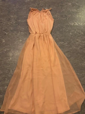 Lång ljusbeige klänning med spetsdetaljer - Superfin långklänning i ljusbeige med tunna axelband och spetsdetaljer vid axlarna. Klänningen har markerad midja med resår och ett skirt, flowy yttertyg som ger en romantisk känsla. Perfekt för sommarens alla tillfällen! 