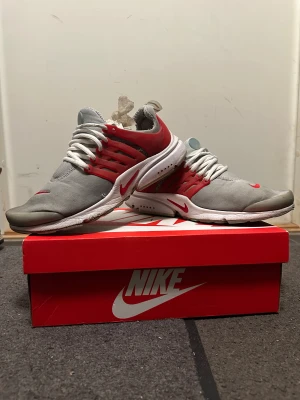 Nike Presto grå/röda sneakers - PRIS KAN DISKUTERAS.                                               Nike Presto sneakers i grått och rött med vita snören och vit sula. Skorna har en sportig design med mesh-överdel och röda detaljer på sidan och häl. Perfekta för dig som gillar en clean och modern look med tydlig Nike-logga på tån och sidan.