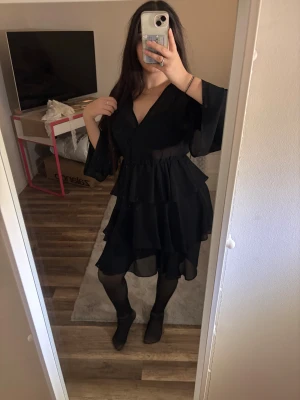Svart omlottklänning med volanger - Säljer en svart kort omlottklänning med v-ringning och volanger i flera lager. Endast använd en gång, ord pris 399kr🥰🤍
