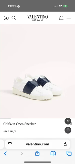 Valentino Garavani Open Sneaker - Snygga vita Valentino Garavani Open sneakers i kalvskinn med en bred marinblå läderdetalj över mitten. Klassisk låg modell med rund tå, platt sula och diskret logga på plösen. Perfekta för dig som vill ha en clean men lyxig look.