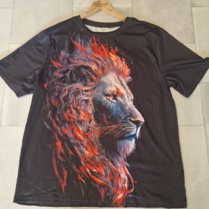 Svart t-shirt med eldlejontryck - Cool svart t-shirt med ett stort, detaljerat tryck av ett lejon med eldliknande man i rött och orange på både fram- och baksidan. T-shirten har rund hals och korta ärmar. Materialet känns mjukt och lätt, perfekt för dig som vill sticka ut med ett unikt motiv.
