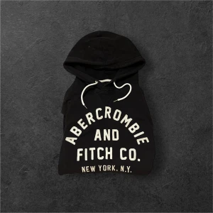 Svart hoodie Abercrombie & Fitch S - Svart hoodie från Abercrombie & Fitch med stor vit logga och text 'New York, N.Y.' på bröstet. Klassisk huva med vita snören och känguruficka framtill. Mjuk bomullsmix som är skön mot huden och perfekt för chill dagar.