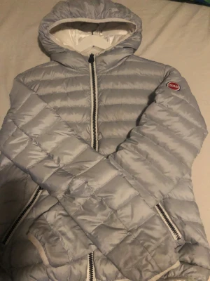 Ljusgrå Colmar dunjacka med huva - Säljer en ljusgrå dunjacka från Colmar med huva och snygga logopatchar på ärmen och ryggen. Jackan har quiltad design, dragkedja framtill och två sidofickor med dragkedja. Perfekt för kalla dagar och har en clean, modern look. Priset inte huget i sten skriv gärna om frågor och om intresserade men även om priset.