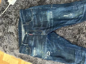 Dsquared2 blå jeans med färgstänk - Säljer ett par äkta jeans från Dsquared2 med coola färgstänk i vitt och gult samt slitna detaljer och patch på bakfickan. Jeansen har klassisk femficksdesign, normal passform. köpta från farfetch för 5500kr