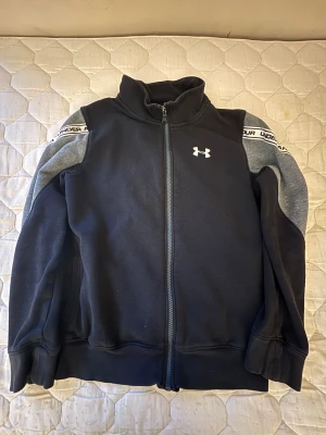 Under Armour ColdGear-jacka - Stilren Under Armour ColdGear-jacka i svart med snygga grå detaljer och branded tape längs ärmarna — perfekt för kyligare dagar! Hög komfort, bra passform och kvalitetskänsla rakt igenom.  ⭐️ Skick: 8/10 – knappt använd, ser riktigt fräsch ut 🎲 Storlek: XS 🎨 Färg: Svart & grå 📦 Skickas snabbt och packas omsorgsfullt