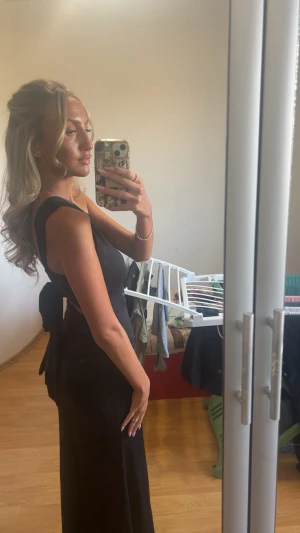 Svart långklänning med rosett i ryggen - Säljer en elegant svart långklänning med breda axelband och snygg rosett i ryggen. Klänningen har en stilren, figurnära passform och är ärmlös, vilket ger en modern och chic look. Perfekt för dig som vill sticka ut med en enkel men sofistikerad stil. Är inte säker på storleken men passar xs och S