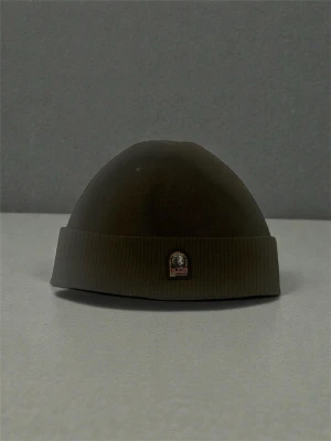 Olivgrön mössa från Parajumpers - Snygg olivgrön mössa från Parajumpers med ribbad kant och klassisk logga framtill. Perfekt för att hålla värmen och addera lite streetstyle till din look. Materialet är mjukt och stretchigt för skön passform. Passar även till båda kön och passar alla där storleken är one size. Den här mössan går för 250 kr men kan förhandlas.