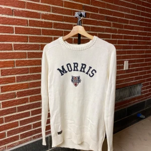 Vit stickad tröja från Morris - Snygg vit stickad tröja från Morris med broderad logga och text på bröstet. Tröjan har rund halsringning, långa ärmar och ribbade muddar. Perfekt för dig som gillar klassisk och stilren look.