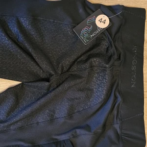Svarta ridleggings från Kingston, stl 44 - Snygga svarta ridleggings från Kingston med diskret mönstrad silikongrip på sätet och låren för extra grepp. Hög midja och stretchigt material som ger en bekväm passform. Perfekta för ridning och träning, med logga längs benet.