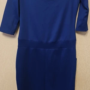 Kornblå klänning med trekvartsärm XL - En stilren kornblå klänning i slät polyester med trekvartsärm och markerad midja. Modellen är knälång och har diskreta fickor i sidorna. Perfekt för dig som gillar enkel men snygg design och vill ha något som sticker ut i färgen.