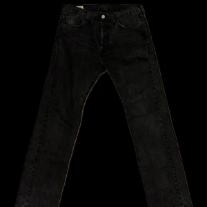 Levi's 501 svarta jeans 32/32 - Svarta Levi's 501 jeans med klassisk rak passform och knappgylf. Jeansen har fem fickor och är tillverkade i slitstarkt denim. Perfekta för dig som gillar en tidlös och clean look. Märke på bakfickan och läderpatch i midjan.