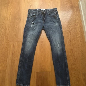 Replay Anbass jeans, blå slim fit - Säljer ett par Replay Anbass jeans i blå tvätt med slitningar och snygga detaljer. Modellen är slim fit med klassisk femficksdesign och dragkedjegylf. Jeansen har en något mörkare blå ton och är tillverkade i mjukt jeanstyg för en skön passform. 