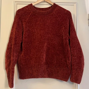 Röd stickad tröja från KappAhl - Mysig röd stickad tröja från KappAhl i mjukt material. Tröjan har rund halsringning, breda ribbade muddar och lång ärm. Perfekt för lager-på-lager under kyliga dagar.