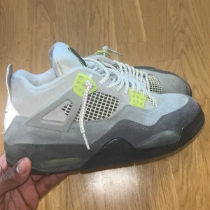 Nike Air Jordan 4  - Nike Air Jordan 4 sneakers i grå mocka med svarta och neongula detaljer. Skorna har vit mesh, reflekterande element och klassisk Jumpman-logga på plösen. Snygga snören med reflex och robust sula. Perfekta för dig som vill sticka ut med en unik streetstyle.