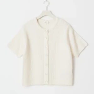 Kortärmad beige kofta med knappar - Superfin kortärmad kofta i beige stickat material med rund hals och knäppning framtill. Perfekt att slänga över ett linne eller t-shirt för en chill och stilren look. Koftan har en mjuk känsla och passar till både jeans och kjol. Xs/s