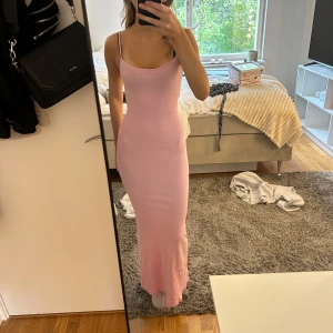 Ljusrosa långklänning med smala axelband - Supersnygg ljusrosa långklänning med smala axelband och figurnära passform. Klänningen är ribbad och har en enkel, stilren design som framhäver siluetten. Perfekt för dig som gillar en feminin och trendig look.