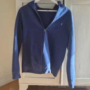 Blå hoodie från Polo Ralph Lauren XL - Säljer en blå hoodie från Polo Ralph Lauren i storlek XL i barn storlek men passar som XS herr storlek. Tröjan har dragkedja framtill, huva och fickor. Klassisk design med broderad logga på bröstet och mjukt bomullsmaterial. Perfekt för chill dagar eller när du vill ha en enkel och snygg look. Skriv vid minsta fundering!!