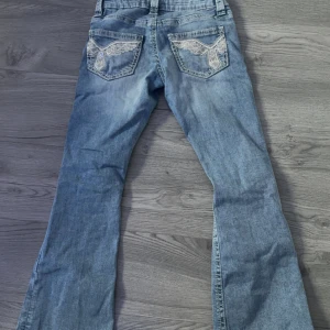 Bootcut jeans från Gina Tricot, ljusblå - Ljusblå bootcut jeans från Gina Tricot med slitna detaljer på benen och snygga broderade bakfickor. Klassisk femficksmodell i jeansmaterial, perfekt för dig som gillar en avslappnad och trendig look.