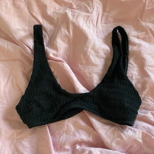 Svart bikiniöverdel från H&M - Svart bikiniöverdel från H&M i smockad modell med breda axelband. Toppens tyg är stretchigt och har en snygg struktur som ger en cool vibe. Perfekt för stranden eller poolen, enkel att matcha med olika underdelar.