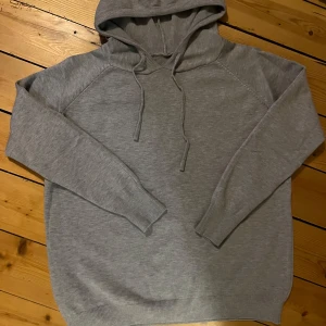 Grå kachmir hoodie  med snörning - En stilren grå hoodie med huva och snörning. Tröjan har långa ärmar, ribbade muddar och är tillverkad i mjuk bomullsmix. Perfekt för chill dagar eller när du vill ha en enkel och clean look.