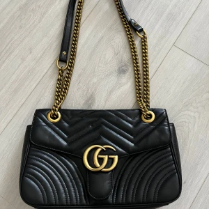 Svart Gucci Marmont axelväska i skinn - Säljer en svart Gucci Marmont axelväska i mjukt skinn med guldfärgade kedjor och GG-logo framtill. 