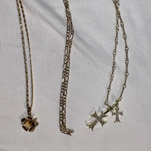 Guldiga halsband med hängen - Tre snygga guldiga halsband med olika kedjor. Ett halsband har ett blommigt hänge, de andra har korshängen och den sista är ett figaro halsband. Kan diskutera pris! 