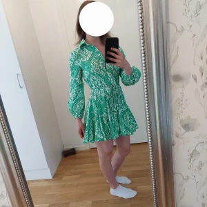 Grönvit blommig kortklänning Zara passar M/S (XS) - Supersöt kortklänning från Zara i storlek XS med grönt och vitt blommönster. Passar personer med Medium/Small. Jag är 167cm och väger 62kg. Klänningen har lång ärm, markerad midja och volangig kjol. Snygg krage och knappar framtill. Perfekt för dig som gillar färg och mönster!