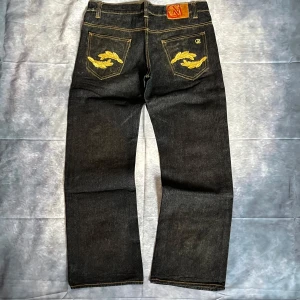 Cavi Raw Denim Jeans – Embroidered Pockets Y2K Streetwear -  Rare Cavi raw denim jeans with bold gold embroidery on the back pockets and inside waistband detail. Classic Y2K streetwear style – premium heavyweight denim with a straight leg fit.  W34/L32  Waist: 43 Hips:46,5 Back rise: 30 Thigh: 31 Knee: 24 Leg opening 24,5 Inseam 78 Outseam 101  Condition: Pre-loved, some natural wear (see pics), but overall great shape for age.  💥 A true statement pair for collectors of 2000s streetwear.  #CaviJeans #Y2KStyle #EmbroideredDenim 