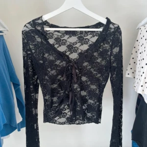 Svart spetsblus med snörning - Säljer en svart, transparent spetsblus med långa ärmar och croppad passform. Blusen har v-ringning och snygg snörning framtill som ger en trendig look. 