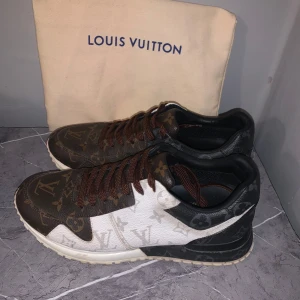 Louis Vuitton run away - Snygga Louis Vuitton sneakers med klassiskt monogrammönster i brunt, vitt och svart. Skorna har bruna snören, rund tå och platt sula. Tillverkade i skinn med tydliga LV-loggor och blommor över hela skon. Perfekt för dig som vill sticka ut med lyxig streetstyle. Möts upp i Sthlm kvitto medföljer 