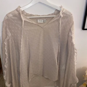  blus från Vila - Supersöt beige blus från Vila med diskret prickigt mönster och volangdetaljer längs ärmarna. Blusen har v-ringning, transparent tyg och långa ärmar. Passar storlek S-M och har inte defekter. Vet inte riktigt va man ska säga att de är för färg. Köpt för typ 400 kr 
