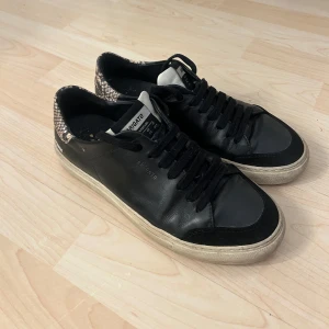 Svarta sneakers från Axel Arigato - Svarta sneakers från Axel Arigato i skinn med coola detaljer i ormskinnsmönster på hälen. Klassisk låg modell med svarta snören. Perfekta för dig som vill ha en stilren men ändå unik look. Köpta för längesedan så tror inte dom finns kvar, knappt använda så mkt bra skick!! Pris kan diskuteras 💕