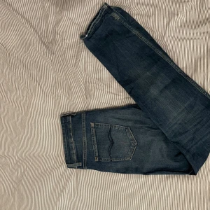 Replay Marty - Säljer ett par mörkblå jeans med klassisk femficksdesign och raka ben. Jeansen har snygga slitningar och kontrastsömmar på bakfickorna. Perfekta för dig som gillar en enkel och tidlös look. Materialet är robust denim som håller länge. 28/32