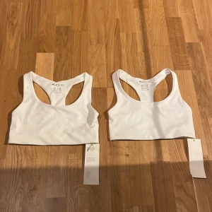 Vita sportiga linnen från MOVE - Två vita sportiga linnen från MOVE med brottarrygg och stilren design. Perfekta för träning eller chill dagar. Gjorda i stretchigt syntetmaterial som sitter skönt och följer kroppen. Säljes med originaltaggar kvar.
