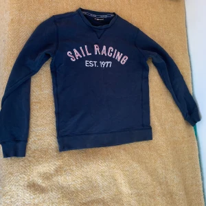 Marinblå Sail Racing sweatshirt - 🚨Pris kan diskuteras 🚨Snygg marinblå sweatshirt från Sail Racing med tryck 'SAIL RACING EST. 1977' på bröstet och logga i nacken. Tröjan har rund hals, långa ärmar och är gjord i mjuk bomull. Perfekt för dig som gillar stilren och sportig look.