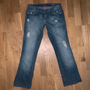 Blue Cult bootcut jeans blå - Snygga blå jeans från Blue Cult med bootcut-modell och slitna detaljer framtill och på bakfickorna. Klassisk femficksdesign, låg midja och cool tvätt. Perfekta för dig som gillar en avslappnad och trendig look.
