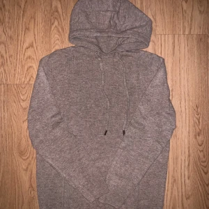 Beige Kashmir  hoodie med huva - Mysig beige Kashmir stickad hoodie med huva och snörning. Tröjan har långa ärmar och ribbade muddar vid ärmslut och nederkant. Perfekt för kyliga dagar när du vill vara både bekväm och stilren.