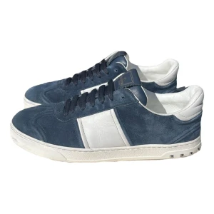 Valentino flycrews - Snygga Valentino Garavani sneakers i blå mocka och vitt skinn. Skorna har svarta snören, silverfärgade nitar på hälen och cool sula med camouflage-mönster. Perfekt för dig som vill sticka ut med exklusiva detaljer och lyxig känsla.