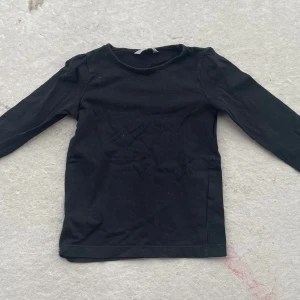 Svart långärmad tröja från Lindex - En enkel svart långärmad tröja från Lindex Kids i mjuk bomull. Tröjan har rund halsringning och en rak passform, perfekt att matcha med jeans eller kjol. Stilren och lätt att bära till olika outfits.