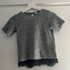 Grå glittrig topp med spetskant Lindex - Säljer en gråmelerad topp från Lindex med glittriga inslag och korta ärmar. Toppen har en snygg svart spetskant nertill som ger en extra detalj.❣️