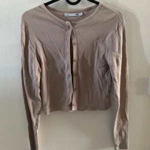 Beige ribbad kofta med knappar - Säljer en beige ribbad kofta från Lager 157 med rund halsringning och långa ärmar. Koftan har knäppning framtill med små knappar och är i ett mjukt bomullsmaterial. Perfekt nu i höst med ett linne under. I storlek S och använd endast en gång. (Kan stryka innan försäljning, legat i en låda därför skrynklig)🤍