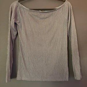glittrig ribbad långärmad topp - Säljer en ”blå” långärmad topp med smala vertikala ränder och ribbad struktur. Toppen har en enkel, rak passform och bred halsringning. Perfekt för dig som gillar stilrena basplagg med lite textur.