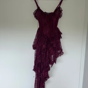 Asymmetrisk spetsklänning - En mörkröd nästan lila klänning helt i spets med en insydd underklänning. Helt oanvänd för att den är lite mindre än den faktiska storleken så den passade inte mig. Den är väldigt snygg då den är kort samtidigt längre på ena sidan.