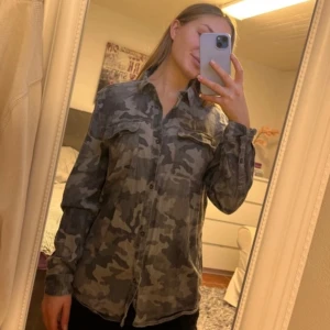 Camouflage skjorta från Zara  - Snygg långärmad skjorta från Zara  i grått camouflage-mönster. Skjortan har klassisk krage, knäppning framtill och två bröstfickor med lock. Perfekt för dig som gillar streetstyle och vill sticka ut lite extra.
