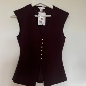 Vinröd väst med guldknappar H&M  - Snygg vinröd väst från H&M i figurnära modell med djup v-ringning och sex guldiga knappar framtill❤️🤗